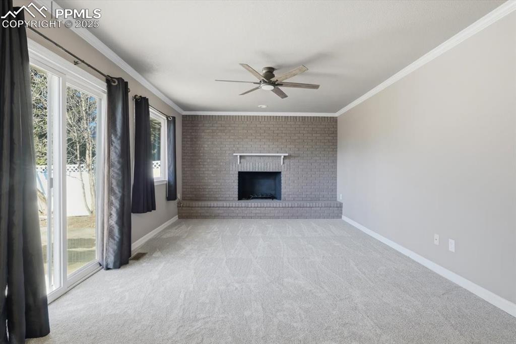 Unfurnished living room with crown molding, light carpet, a brick fireplace, and ceiling fan