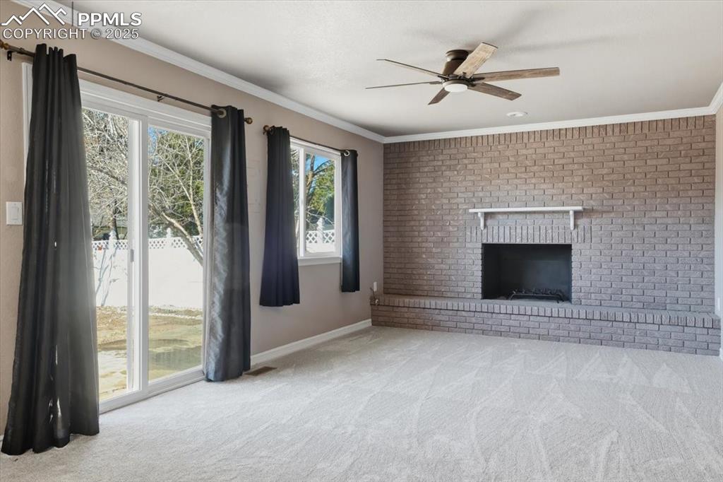 Unfurnished living room featuring ornamental molding, a fireplace, carpet, and a ceiling fan