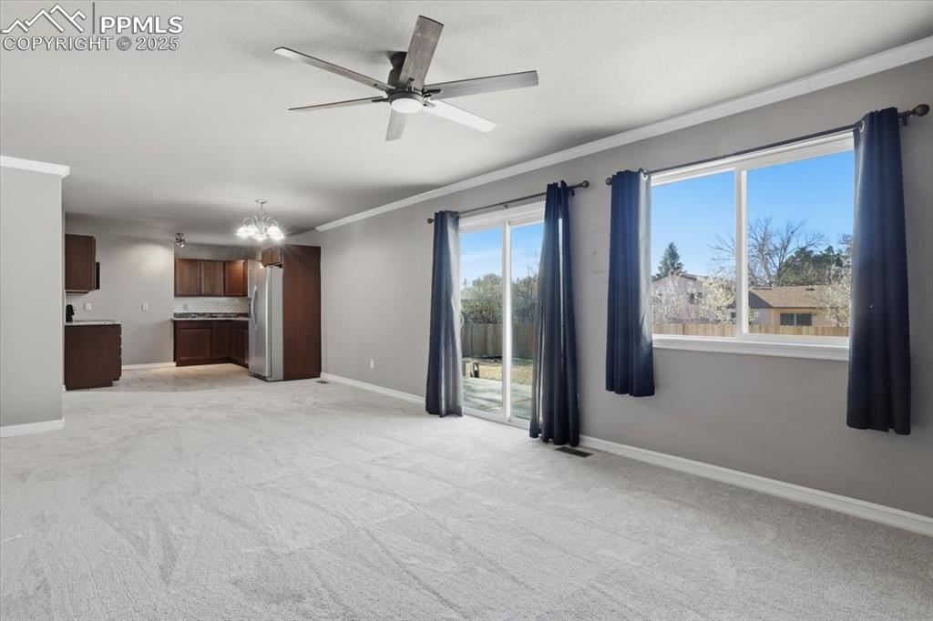 Unfurnished living room with crown molding, a chandelier, ceiling fan, and light colored carpet