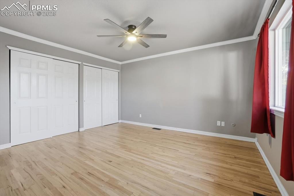 Unfurnished bedroom featuring crown molding, multiple closets, light wood finished floors, and a ceiling fan