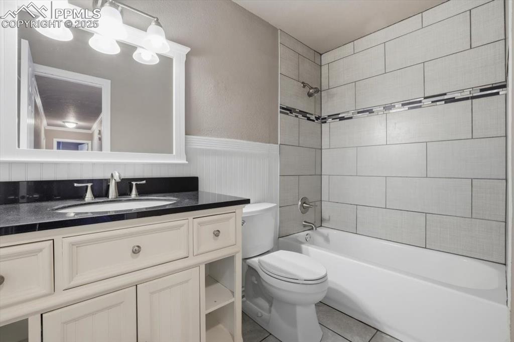 Bathroom with vanity, tub / shower combination, light tile patterned floors, and a wainscoted wall