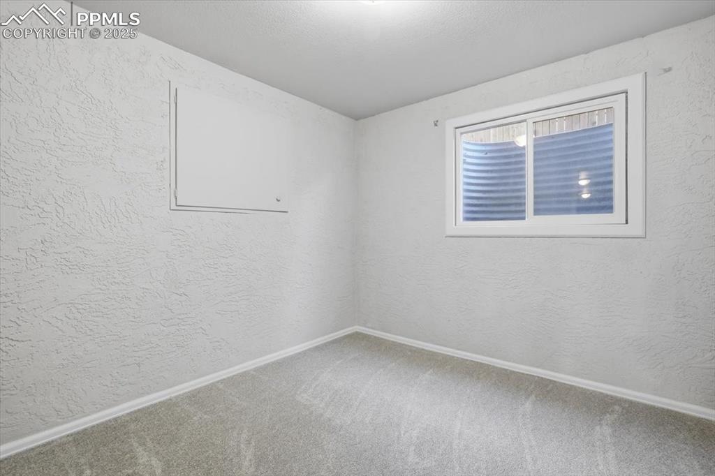 Carpeted spare room with a textured wall and baseboards