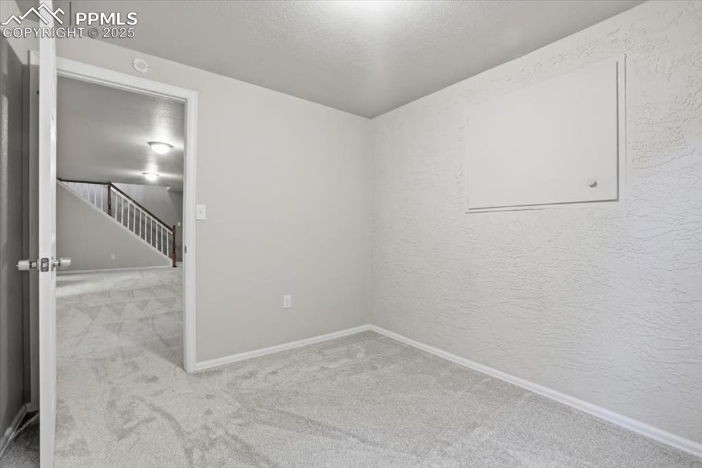 Unfurnished room featuring light colored carpet, stairway, a textured ceiling, and a textured wall