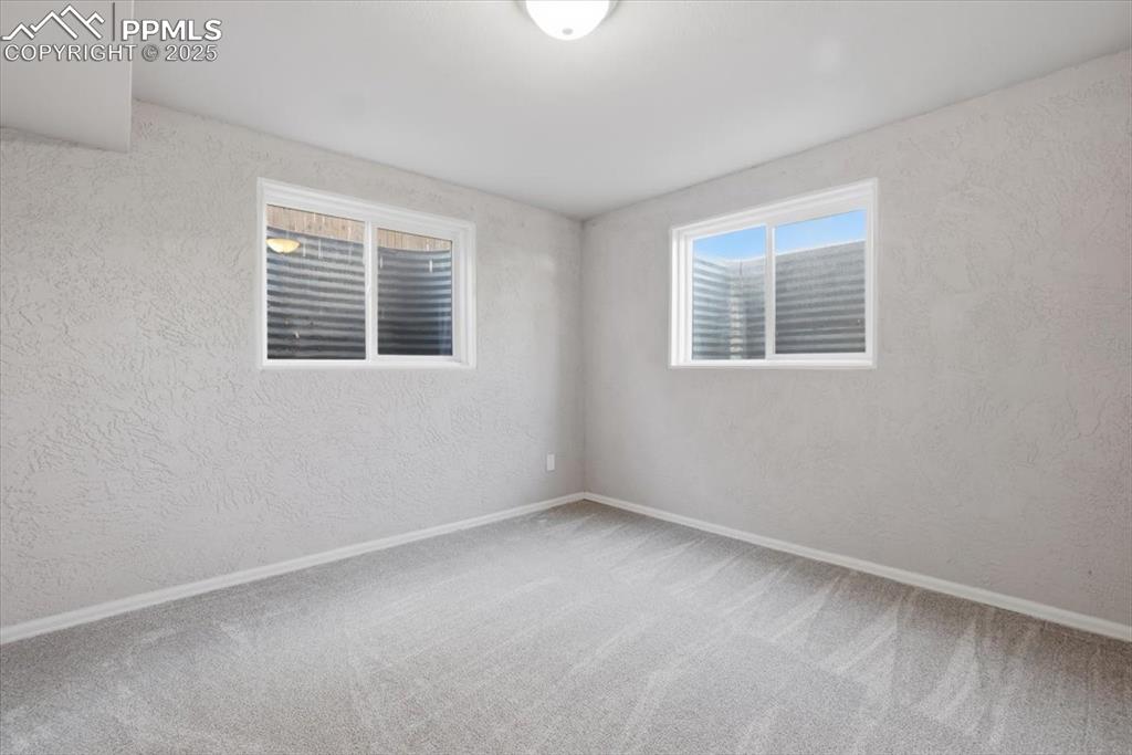 Carpeted spare room featuring a textured wall and baseboards