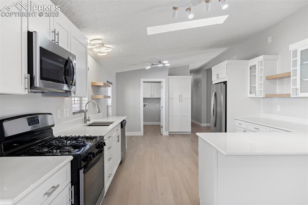 Kitchen with sink, vaulted ceiling, a textured ceiling, appliances with stainless steel finishes, and white cabinets