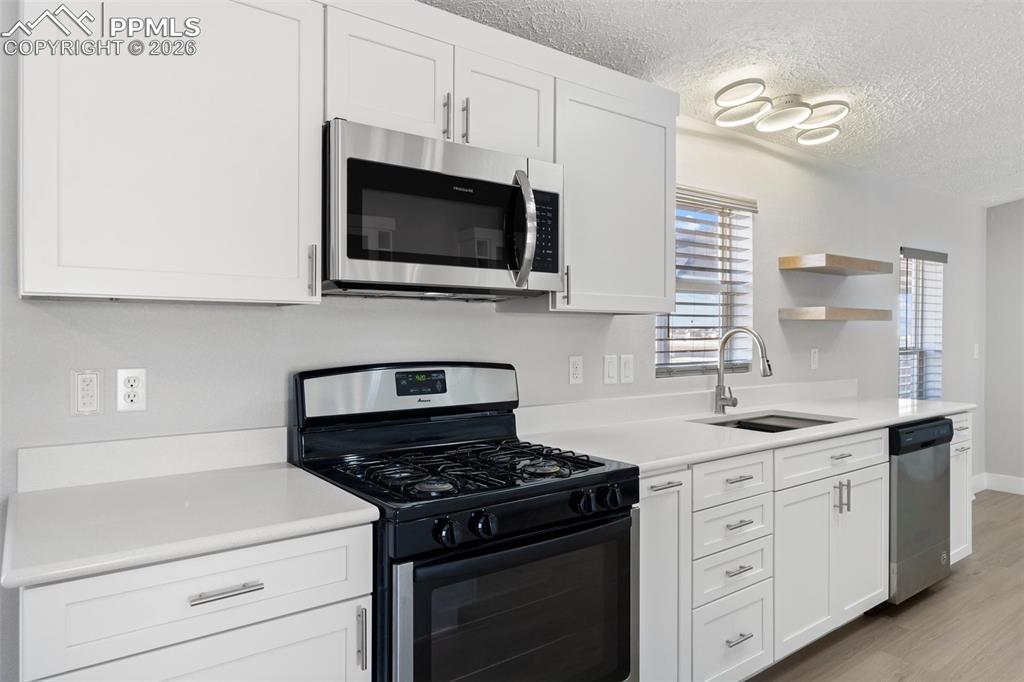 Kitchen featuring stainless steel appliances, sink, white cabinets, and light hardwood / wood-style floors