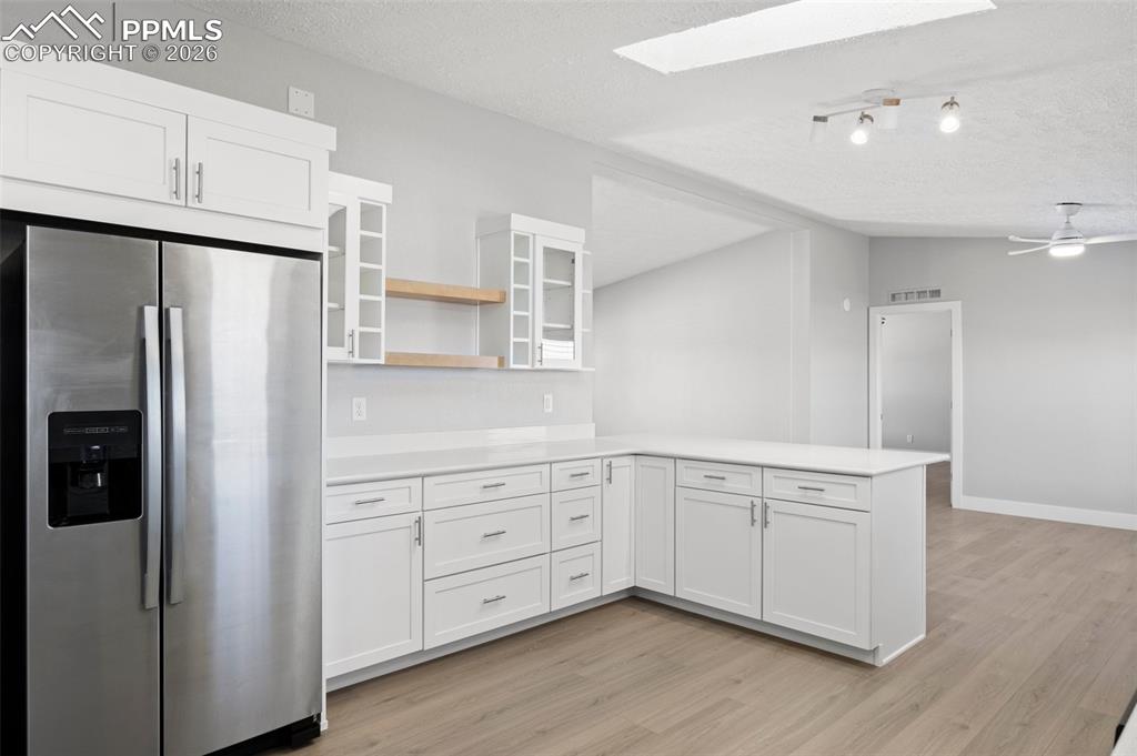 Kitchen with stainless steel fridge, vaulted ceiling with skylight, white cabinets, kitchen peninsula, and light wood-type flooring