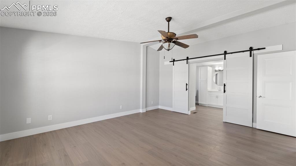 Unfurnished bedroom with hardwood / wood-style flooring, a barn door, connected bathroom, and a textured ceiling