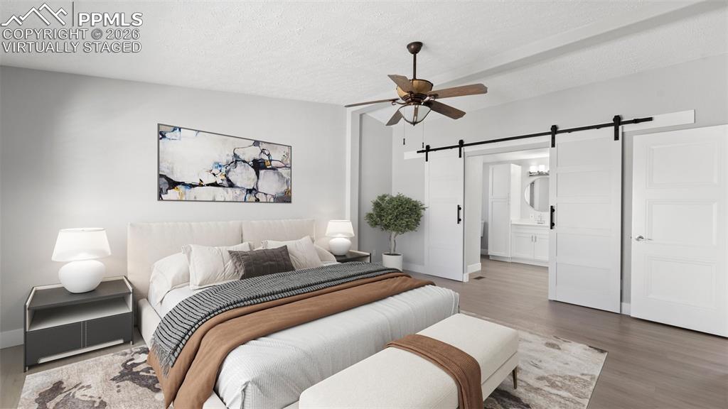 Bedroom featuring ensuite bath, a textured ceiling, ceiling fan, a barn door, and hardwood / wood-style floors--virtually staged Picture 