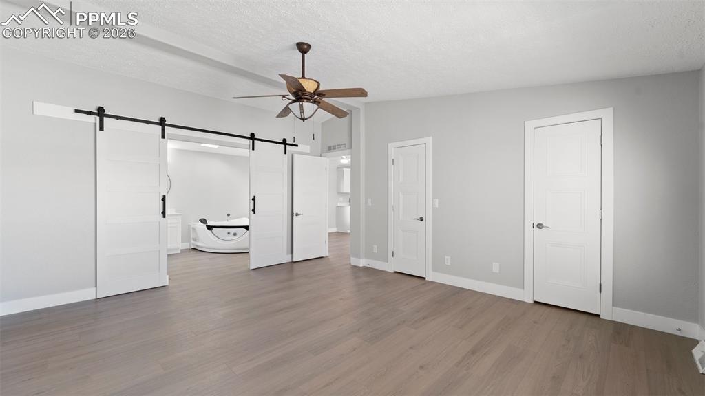 Unfurnished bedroom with hardwood / wood-style flooring, a barn door, vaulted ceiling, and a textured ceiling