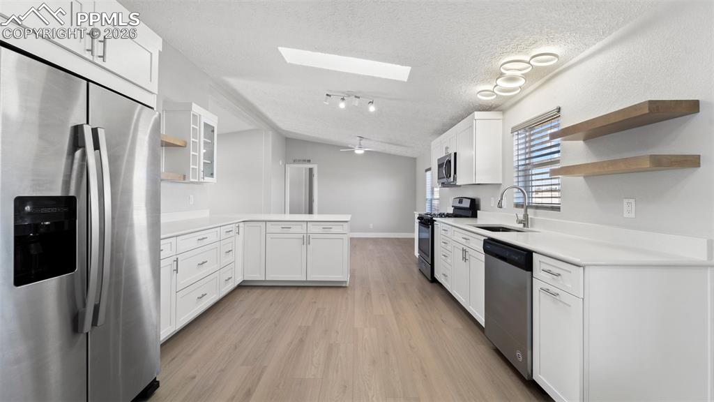 Kitchen featuring sink, white cabinetry, lofted ceiling with skylight, stainless steel appliances, and a textured ceiling
