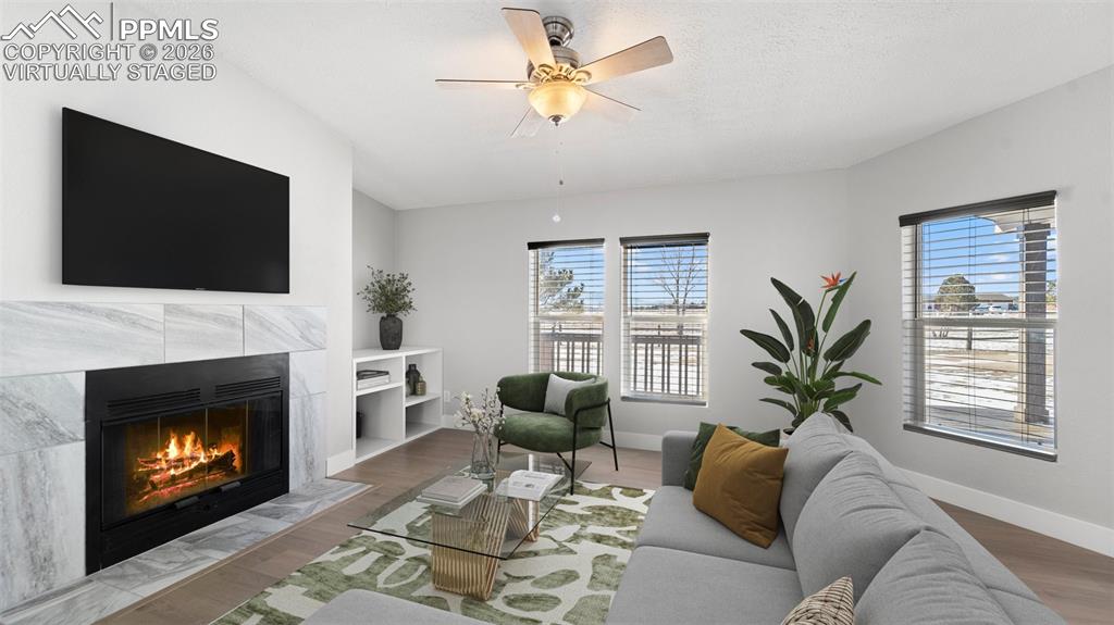 Living room featuring ceiling fan, plenty of natural light, a fireplace, and wood-type flooring--Virtually Staged Picture