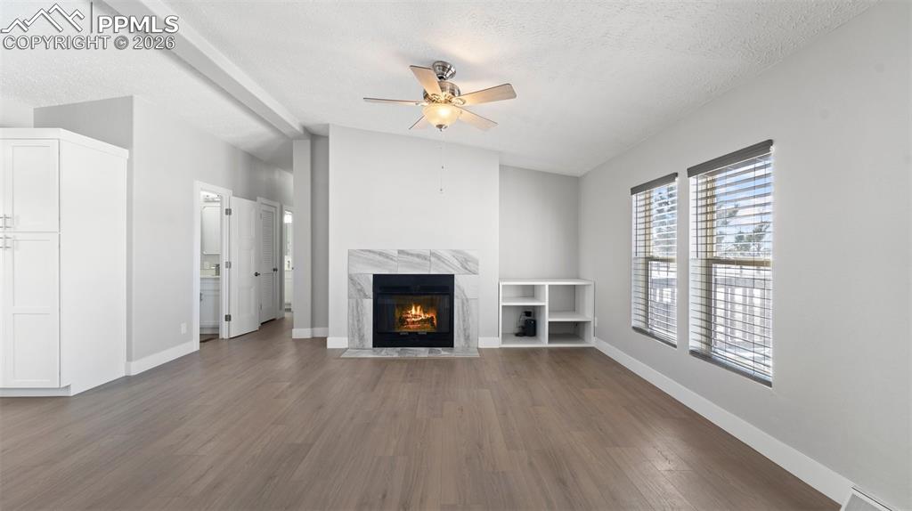Unfurnished living room with lofted ceiling, ceiling fan, hardwood / wood-style floors, a fireplace, and a textured ceiling