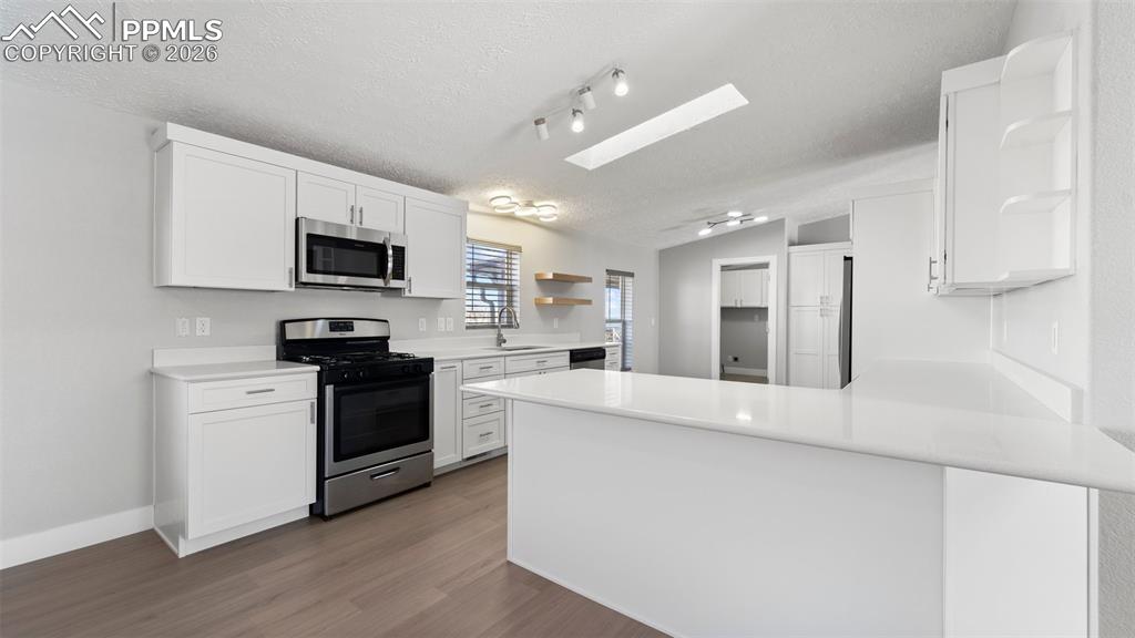 Kitchen with white cabinetry, sink, stainless steel appliances, and kitchen peninsula
