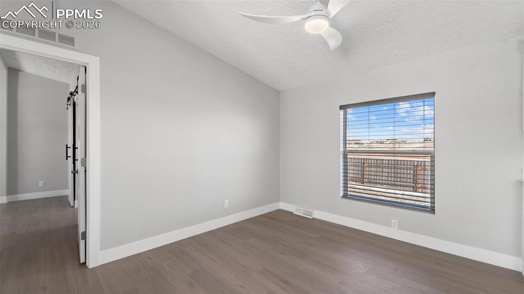 Unfurnished room with ceiling fan, dark hardwood / wood-style floors, a textured ceiling, vaulted ceiling, and a barn door