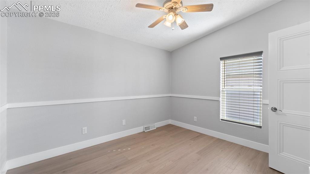 Unfurnished room featuring ceiling fan, lofted ceiling, a textured ceiling, and light wood-type flooring