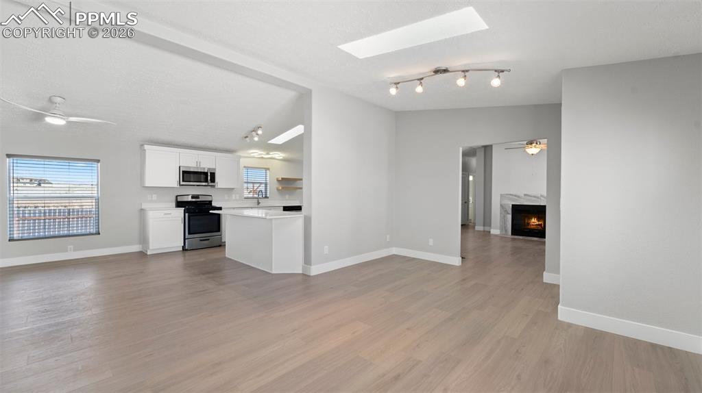 Kitchen with appliances with stainless steel finishes, vaulted ceiling with skylight, white cabinetry, a high end fireplace, and ceiling fan