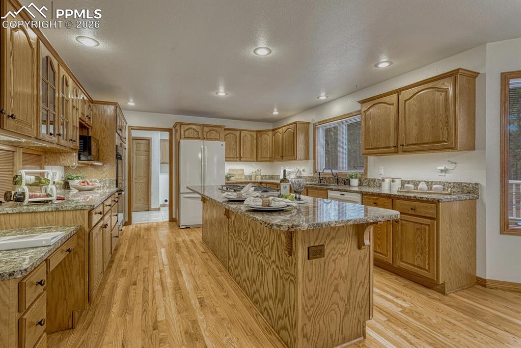 The gourmet island kitchen showcases hardwood floors, rich wood cabinetry, granite countertops, a planning desk, dining nook, and access to an expansive composite deck. 