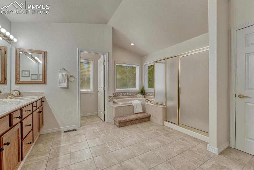 Spa-like adjoining Primary Bathroom with tile floor, dual sink vanity, Jacuzzi tub, and separate shower with built-in seating.
