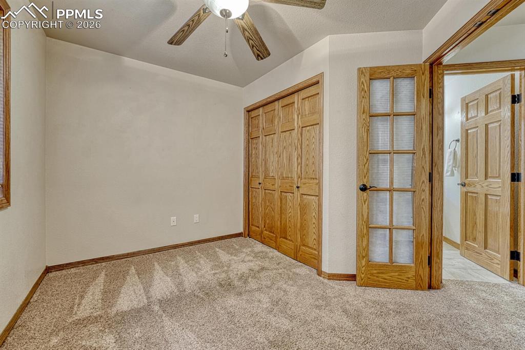 Main level Bedroom/Office with French doors, neutral carpet, lighted ceiling fan, and generous closet.