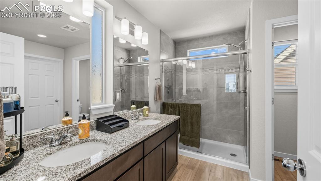 Full bath featuring double vanity, a shower stall, and light wood-style flooring