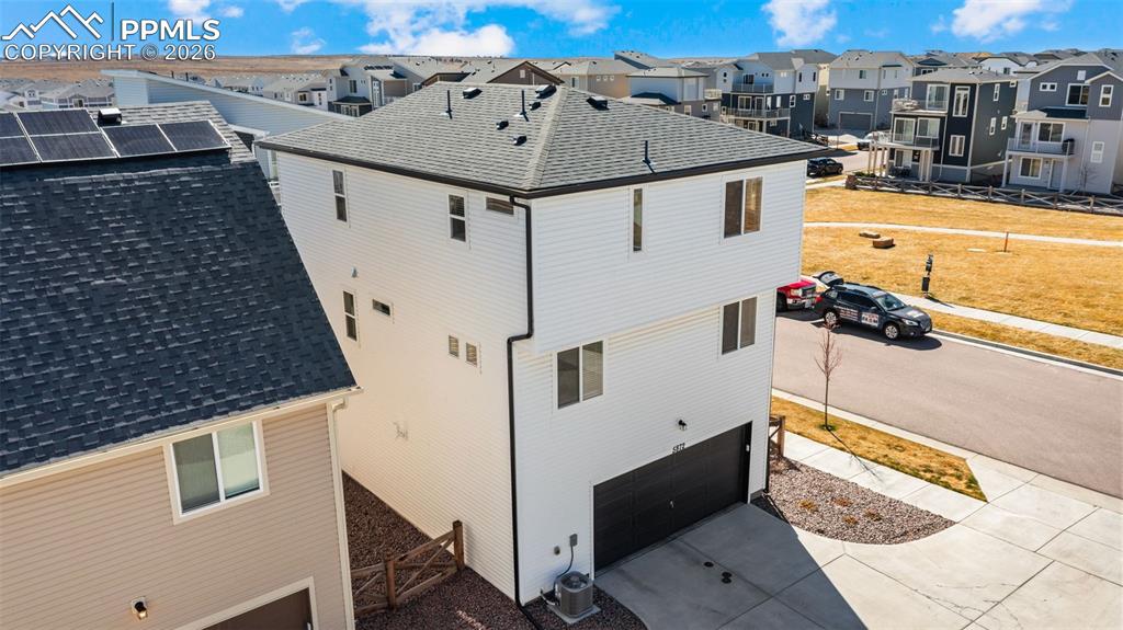 View of side of home with an attached garage, roof with shingles, concrete driveway, and a residential view