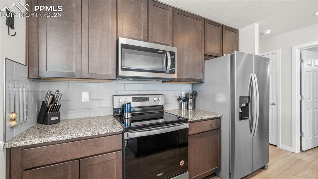 Kitchen featuring stainless steel appliances, light stone countertops, backsplash, and light wood-style flooring