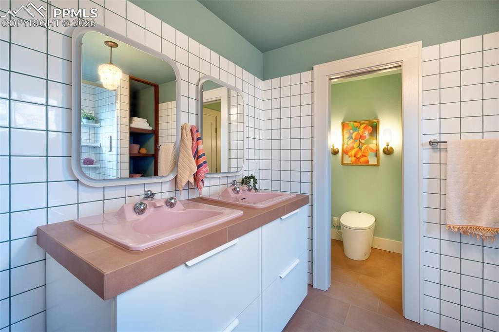 Ensuite primary bathroom, fully remodeled. Separate water closet with Japanese style toilet, custom built double vanity with vintage sinks, custom colored epoxy grout as design highlight along vintage fixtures and built in linen storage.