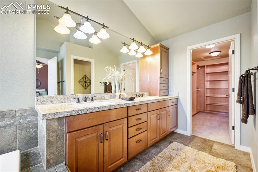 Full bath with double vanity, lofted ceiling, and a spacious closet