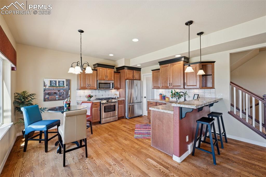 Kitchen with stainless steel appliances, a peninsula, brown cabinetry, a kitchen bar, and light wood-style floors