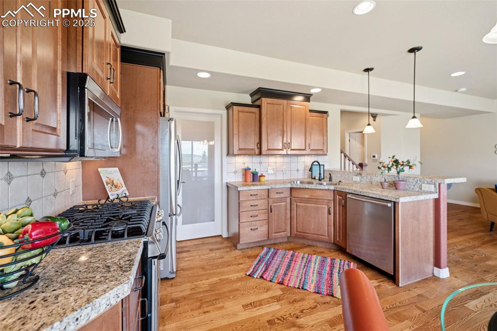 Kitchen featuring stainless steel appliances, a peninsula, light wood finished floors, decorative backsplash, and light stone countertops