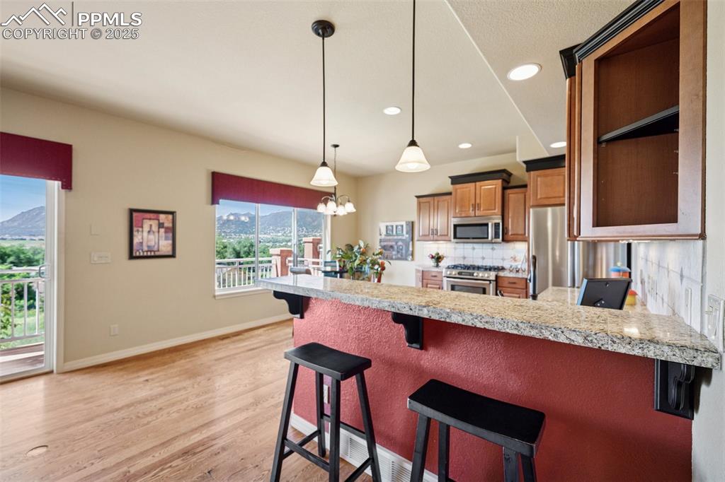 Kitchen with appliances with stainless steel finishes, a peninsula, tasteful backsplash, light wood-type flooring, and recessed lighting