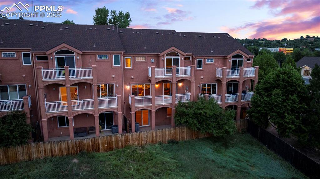 Back of house at dusk featuring stucco siding, a fenced backyard, a balcony, and roof with shingles