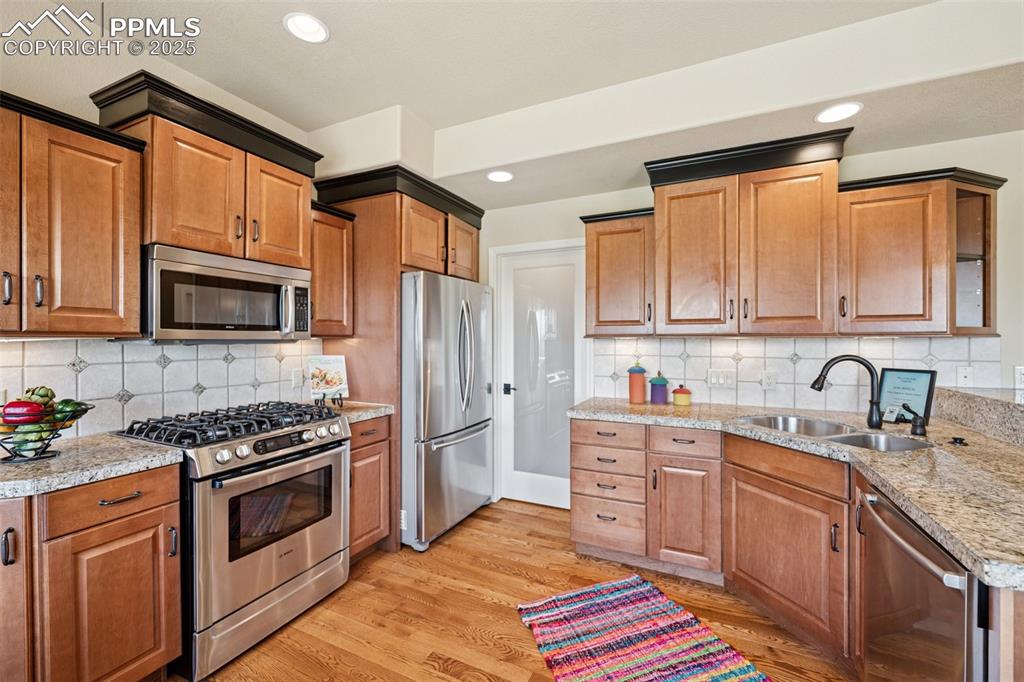Kitchen with appliances with stainless steel finishes, light wood-style flooring, decorative backsplash, light stone counters, and recessed lighting