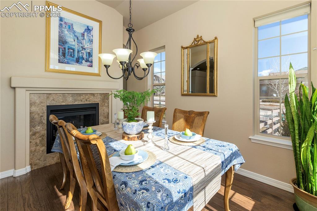 Dining area with dark wood-style flooring, hanging lights, a glass covered fireplace, and lofted ceiling