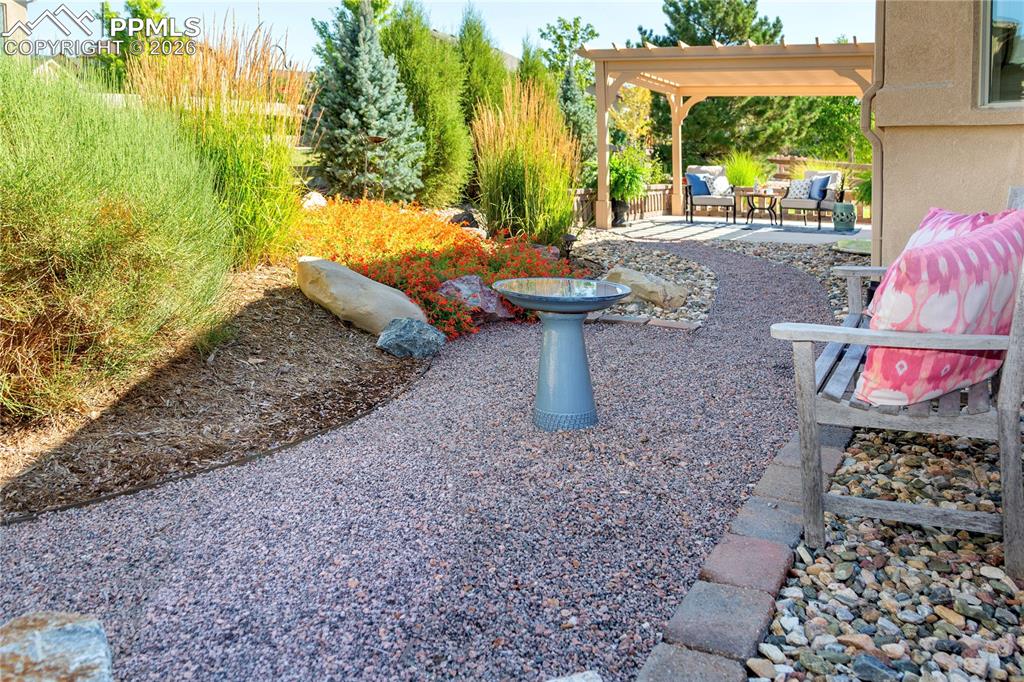 Crushed gravel pathway with boulders, blooming flower beds, pampas grass and blue spruce.