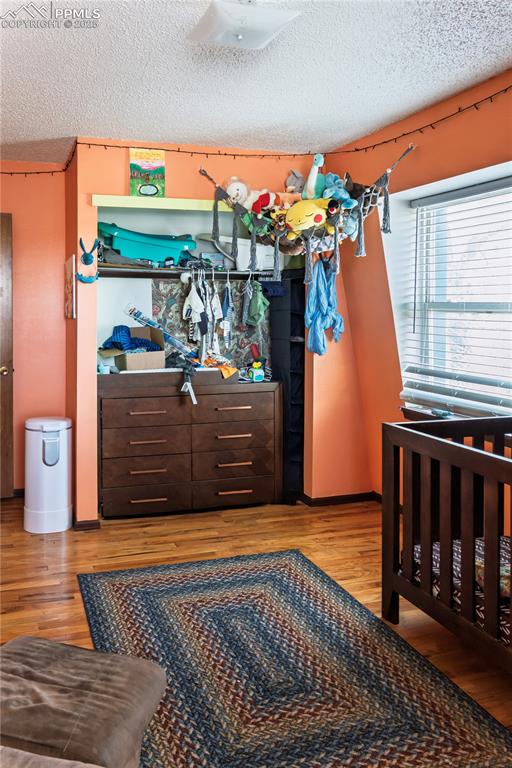Bedroom with a textured ceiling, light wood-style floors, and a nursery area