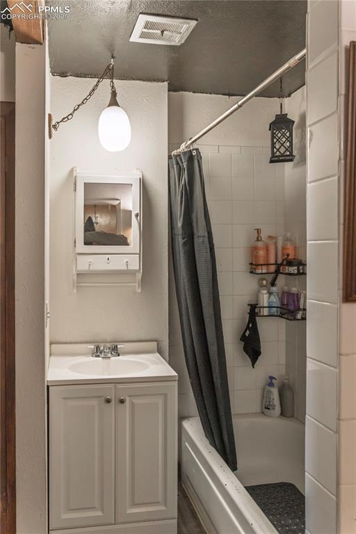 Bathroom featuring vanity, a textured wall, and shower / bath combo