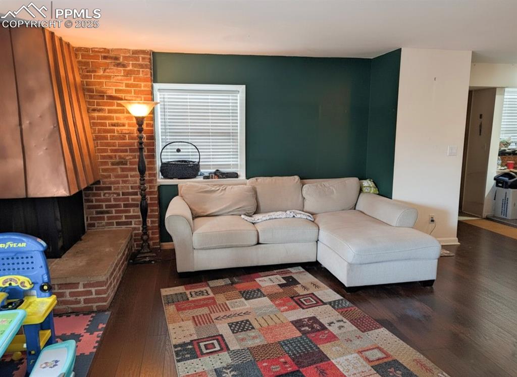 Living room featuring dark wood finished floors, brick wall, and plenty of natural light