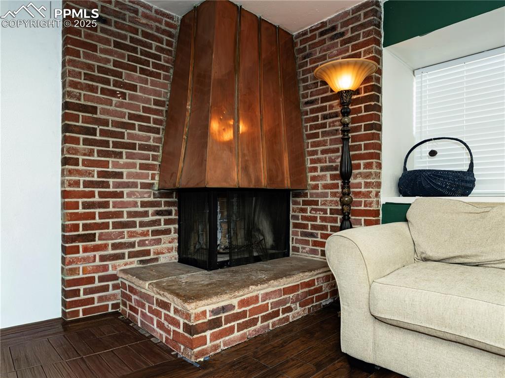Living room with a fireplace, dark wood-type flooring, and brick wall