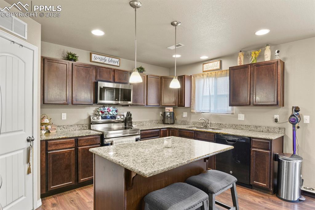 Kitchen featuring stainless steel appliances, a kitchen breakfast bar, dark brown cabinets, light wood finished floors, and recessed lighting
