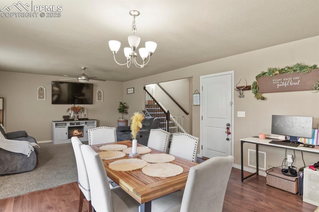 Dining area with a chandelier, ceiling fan, stairs, wood finished floors, and a warm lit fireplace