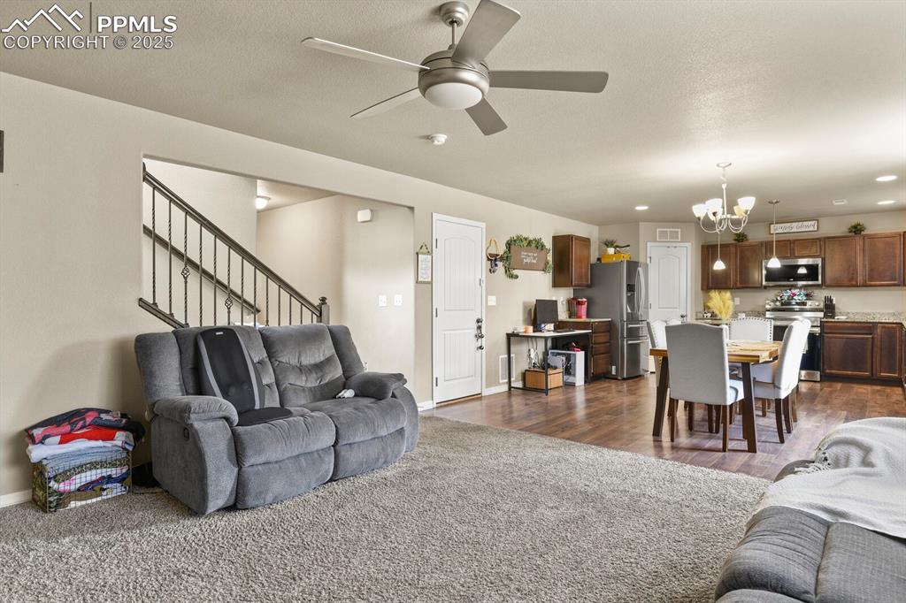 Living room with a chandelier, a ceiling fan, stairs, and dark wood finished floors