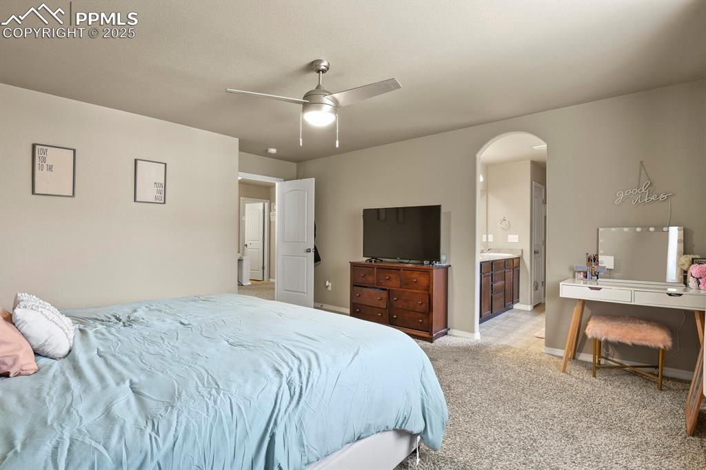 Bedroom featuring arched walkways, light colored carpet, ceiling fan, and connected bathroom