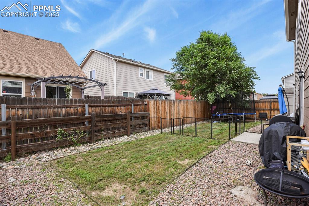 Fenced backyard with a trampoline and a pergola