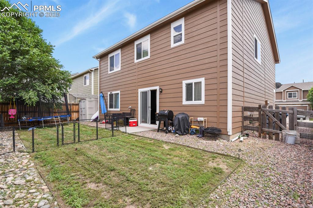Rear view of property featuring a trampoline, a shed, a fenced backyard, a patio, and a gate
