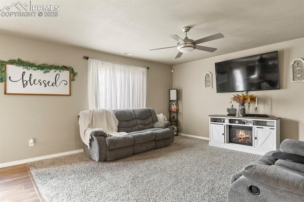 Living room with a ceiling fan, a textured ceiling, and a glass covered fireplace