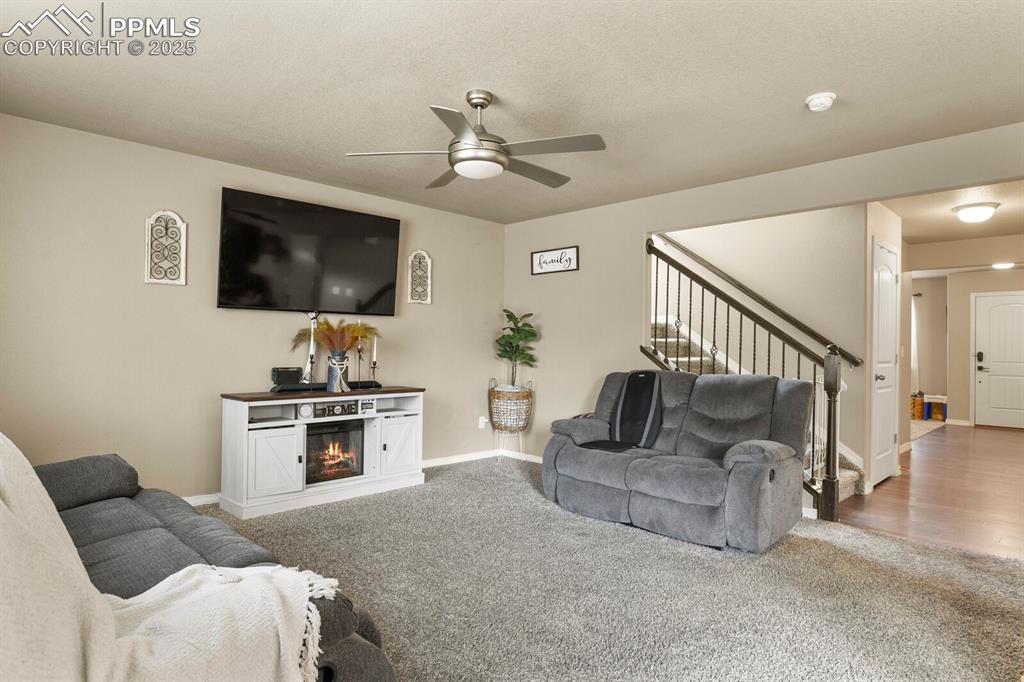 Living area featuring stairs, a ceiling fan, carpet, and a glass covered fireplace