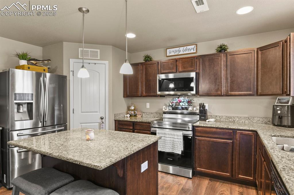 Kitchen featuring stainless steel appliances, a breakfast bar area, wood finished floors, dark brown cabinets, and recessed lighting