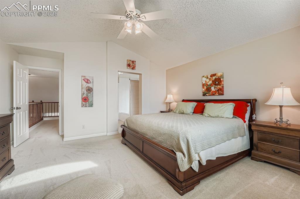 Bedroom with carpet flooring, vaulted ceiling, ceiling fan, and a textured ceiling